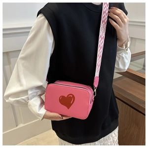 Detail of pink crossbody bag featuring a red heart pattern and wide woven shoulder strap