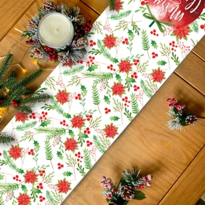 Christmas table runner with red poinsettia and pine needles on light wood tabletop
