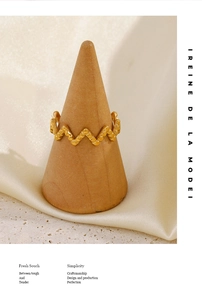 Macro detail of wave-shaped gold ring with grainy texture on wooden display stand