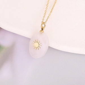 Close-up of gold chain necklace with oval pink stone pendant and sun motif detail
