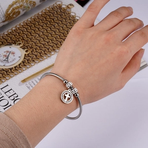 Detail of silver snake chain bracelet featuring a rhinestone cross pendant on wrist