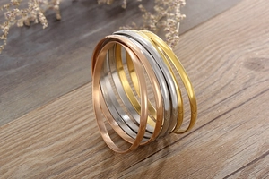 Polished gold, rose gold, and silver titanium steel bangles stacked on a wooden surface