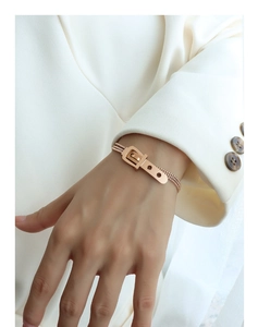 Rose gold mesh bracelet with belt buckle design worn over a white suit sleeve