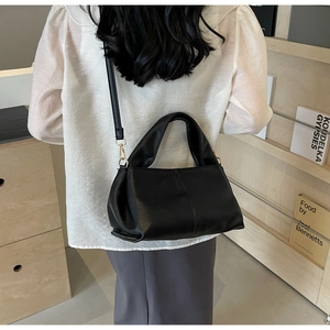 Model wearing a black leather crossbody bag with gold hardware against a cozy wooden interior