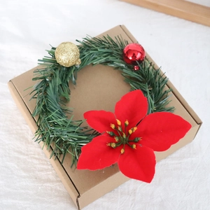 Detailed view of mini Christmas wreath with red poinsettia and gold balls on a gift box