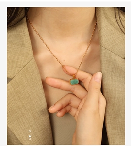 Close-up of golden Amazonite pendant necklace worn by a model on a beige blazer