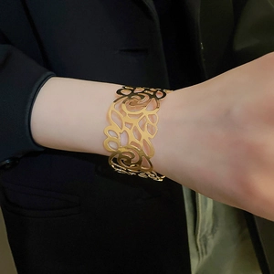 Close-up of a wide gold open cuff bracelet with intricate floral hollow-out patterns