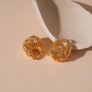Macro detail of gold-plated U-shaped hoop earrings featuring woven texture and metallic luster