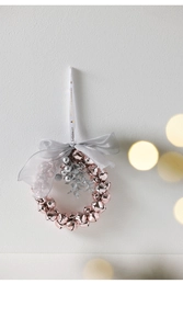 Close-up of rose gold bell wreath ornament with silver bow and Merry Christmas ribbon