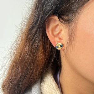 Nahaufnahme eleganter ovaler Goldohrringe mit zwei blauen Zirkonia am Ohrläppchen