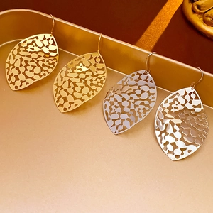 Macro detail of leaf-shaped cutout drop earrings in gold and silver metal finishes