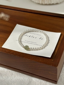 Macro detail of white pearl bracelet with green jade bead on premium wooden jewelry box