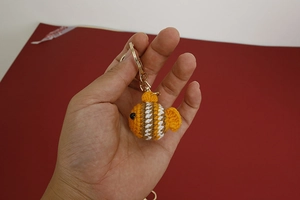 Handheld view of handmade crochet clownfish keychain with golden metal ring and hook