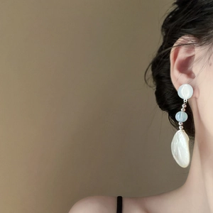 Detail of drop earring with light blue resin bead and large white baroque pearl on model