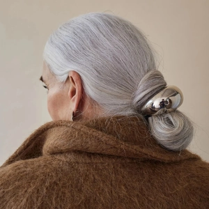 Macro view of a silver-toned streamlined metal hair tie on a model with a minimalist style