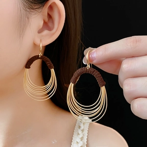 Detail view of layered gold oval hoop earrings with brown thread wrap on model