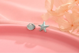 Macro detail of asymmetric starfish and seashell stud earrings with light blue enamel finish