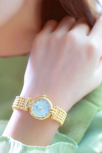 Detail of luxury gold women's watch with rhinestone dial and bead chain strap on wrist
