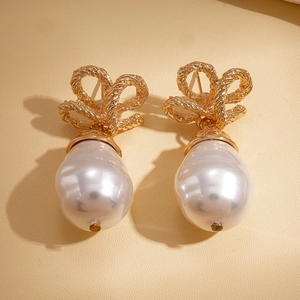 Close-up of golden bow earrings with baroque pearls on a textured cream background