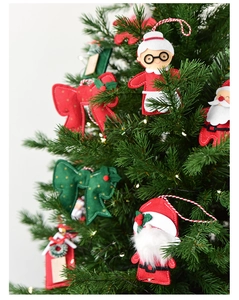 Detail of felt Santa and snow cabin ornaments hanging on a green Christmas tree