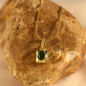 Elegant gold necklace with rectangular emerald pendant on a natural stone background