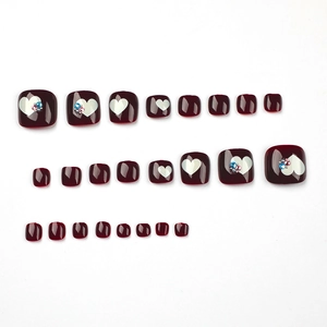 Glossy burgundy press-on toenails with white heart patterns and sparkling rhinestones