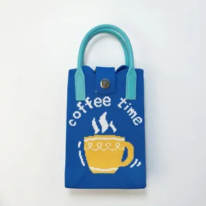 Detail of blue knitted phone bag featuring coffee time pattern and round blue handle