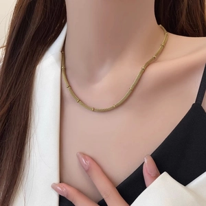 Gold mesh weave necklace with small beads worn by model in a stylish white blazer