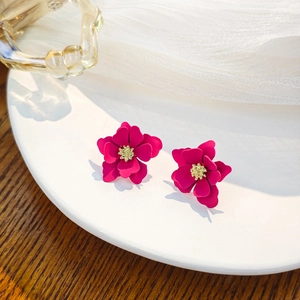 Macro detail of magenta flower earrings with gold stamens on a white ceramic plate