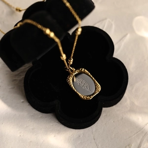 Detail of vintage 18K gold rose pendant necklace inside a black floral velvet jewelry box
