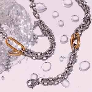 Detail of silver chain with 18K gold-plated oval links on mirror surface with water drops