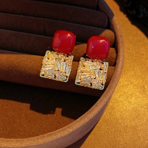 Macro shot of red square stud earrings with clear rectangular zircons on brown velvet
