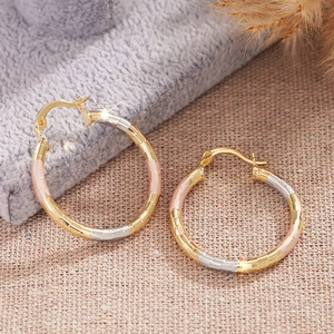 Three-tone gold textured hoop earrings with a faceted bamboo-inspired design on fabric