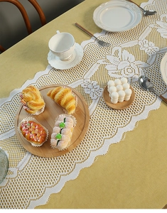 Close-up of white floral lace table runner with hollow design on warm yellow tablecloth