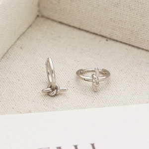 Close-up of S925 sterling silver knot earrings on a beige textured fabric background