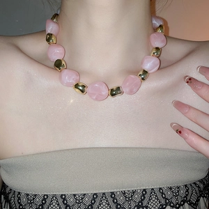 Detail of pink acrylic irregular beads and golden metal spheres on a high-end necklace