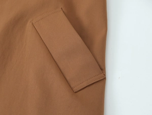 Detail einer braunen Twill-Trenchcoat-Tasche mit sauberer Naht und rechteckiger Klappe