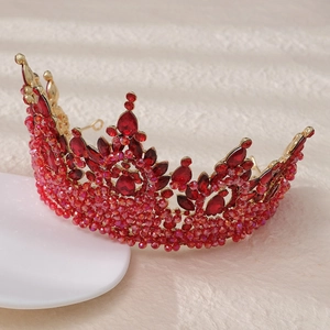 Close-up of golden crown with red faceted rhinestones and beads on white display base