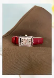 Dettaglio orologio quadrato dorato con quadrante di cristalli e cinturino in pelle rossa