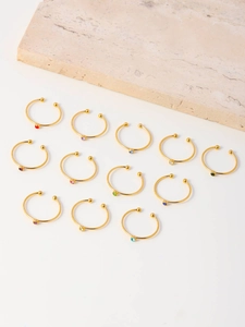 Set of 12 gold plated nose rings with colorful zircon gemstones on a stone display
