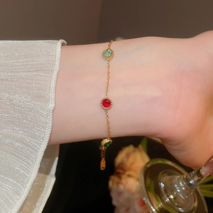 Detail of a gold chain bracelet with red and green gemstones worn by a model in lifestyle setting