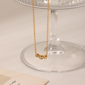 Close-up of gold 18K necklace featuring three bezel-set cubic zirconia on glass stand