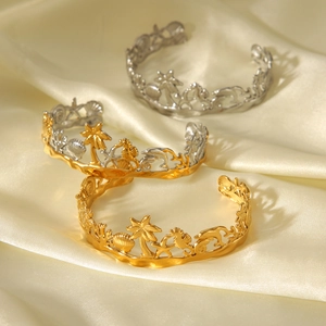Detailed macro view of ocean-themed open bangles with seahorse and shell on silk