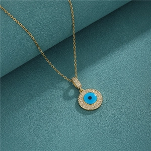 Gold Evil Eye necklace with blue zircon pendant on a textured teal background