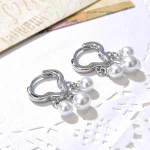 Elegant heart-shaped silver earrings with cascading white pearls on a vintage background