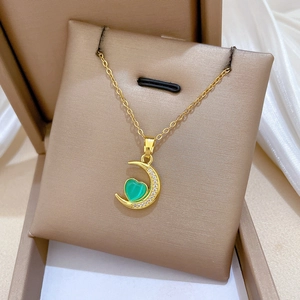 Close-up of a gold crescent moon and green heart pendant necklace in a luxury gift box