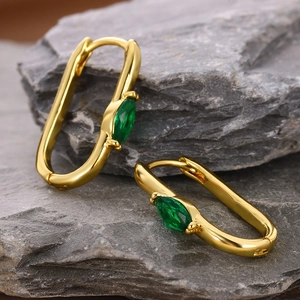 Macro shot of gold oval hoop earrings with emerald zircon on grey stone background