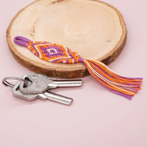 Detailed handmade woven keychain with purple geometric patterns and long tassels on wood