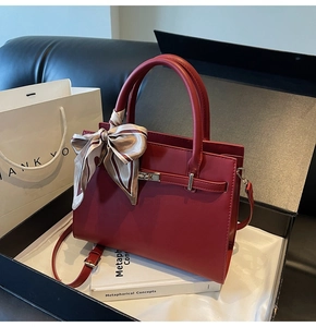 Close-up of deep red leather handbag with silk scarf detail and golden metal buckle
