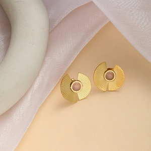 Detail view of gold stud earrings featuring a pink gemstone and radial fan pattern